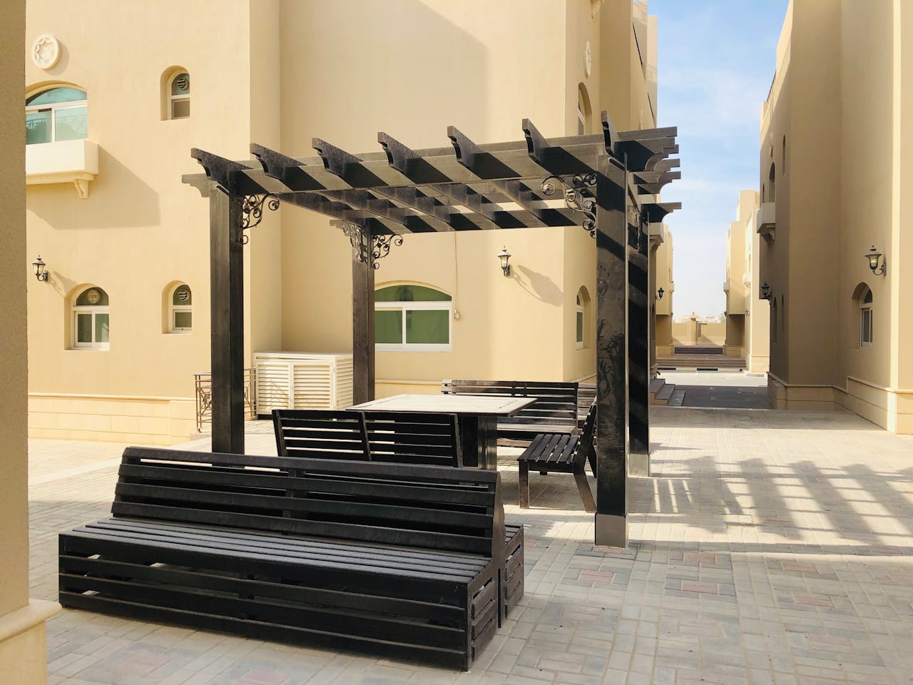 Modern outdoor seating area in an Abu Dhabi alley, featuring pergola and benches.