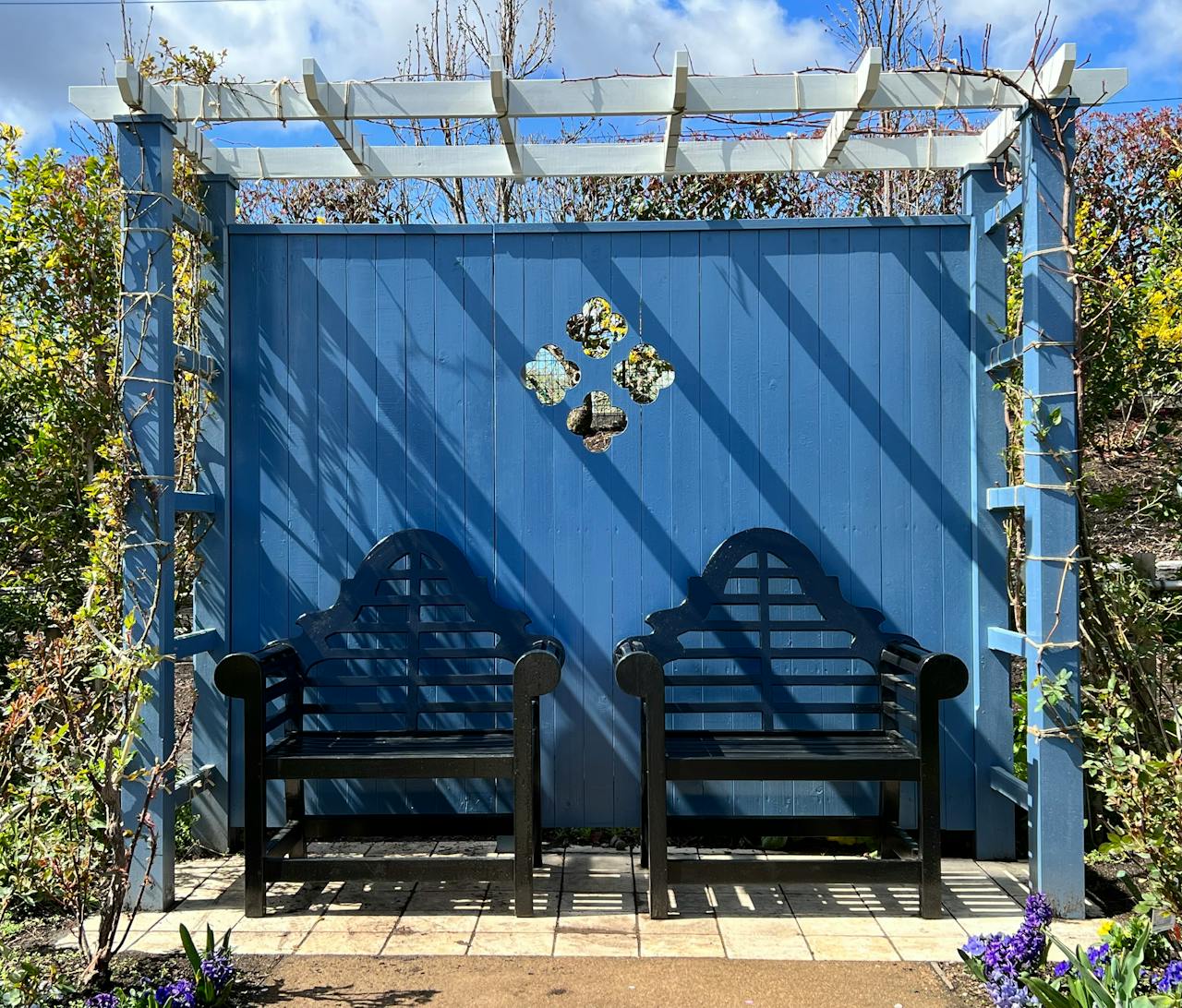 Beautiful garden scene with a blue wooden pergola and black benches under a clear sky.