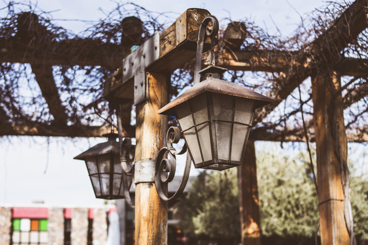 Close-up of vintage lanterns hanging from a wooden pergola in an outdoor setting.